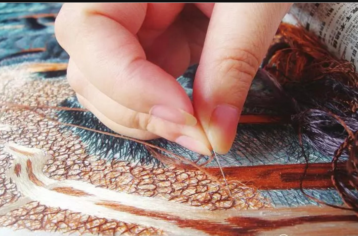 Close-up macro shot of an artisan's hand meticulously stitching fine silk threads, demonstrating the intricate textures of traditional Chinese random-stitch embroidery.