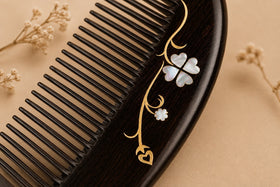 Close-up macro shot of a black ebony wood comb adorned with exquisite mother of pearl inlay and delicate gold floral wire decoration on a soft beige background.