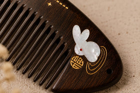 Close-up macro shot of a black ebony wood comb adorned with exquisite mother of pearl inlay and delicate gold floral wire decoration on a soft beige background.